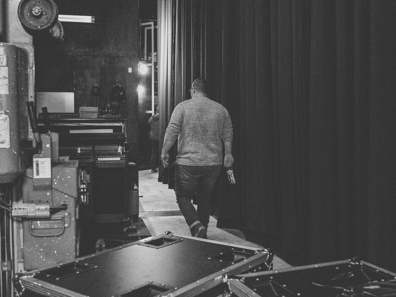 A crew member walking past flight cases behind a stage